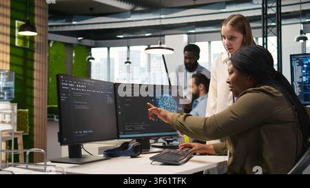 Manager teaching young technician how to develop software and optimize code using AI. Team leader guiding intern in office on how to use artificial intelligence to resolve bottlenecks, camera A Stock Photo