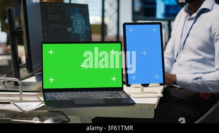 Startup office admin reviewing AI system metrics on isolated screen devices, monitoring performance dashboards. Man tuning neural networks using tools on mockup laptop and tablet, camera A Stock Photo