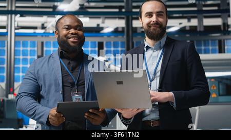 Team of diverse analysts consultants reviewing data and checklists in a high tech solar panel plant, ensuring manufacturing process meets sustainable energy and innovation standards. Camera B. Stock Photo