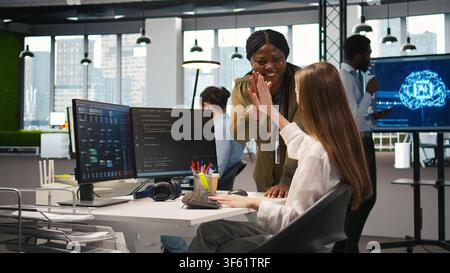Happy manager praising intern progress with encouraging words, doing congratulating high five. Smiling team leader providing positive feedback for young female engineer at work, camera A Stock Photo