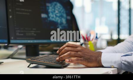 System administrator at office desk developing software applications using AI automation. IT specialist working on computer, debugging applications with artificial intelligence, camera A Stock Photo