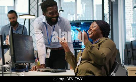 Cheerful programmers in office enjoying conversation while automating repetitive tasks with AI. Happy coworkers chatting, using artificial intelligence to speed up feature implementation, camera A Stock Photo