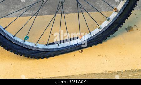 The tire of a bicycle is completely flat, resting on a vibrant yellow curb. This highlights potential issues with maintenance and the need for assista Stock Photo