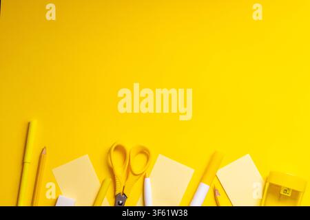Flat lay composition featuring stationery items including scissors, pencils, sticky notes, markers and paper arranged along the bottom edge, leaving a Stock Photo