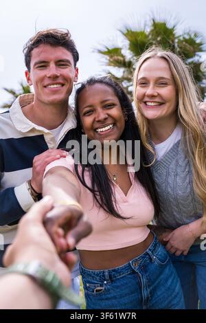 Group of friends walking together candidly, one reaching a hand towards the camera near palm trees Stock Photo