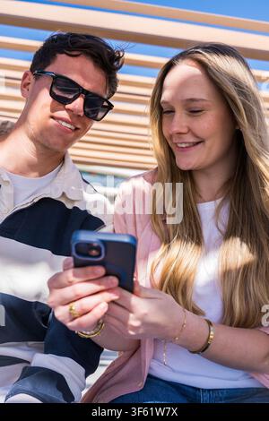 Young couple laughing together while looking at a smartphone screen, sitting close together Stock Photo