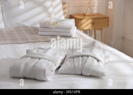 Clean bathrobes with flowers and towels on bed indoors, closeup Stock Photo