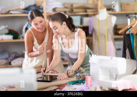 Two female dressmakers drawing a model of clothes on a tablet Stock Photo