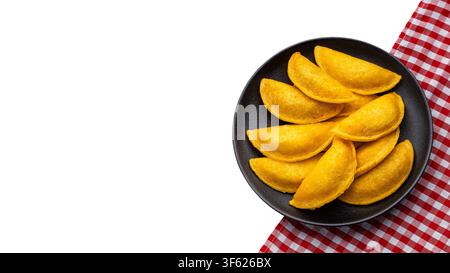 Golden Colombian corn empanadas served on a black plate on a red checkered tablecloth, isolated on a white background with space for text. Ideal for f Stock Photo