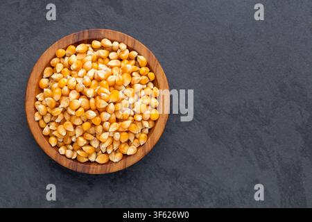 Popcorn kernels in a wooden bowl on a dark background, food photography with space for text, ideal for cooking concepts, snacks, and natural ingredien Stock Photo