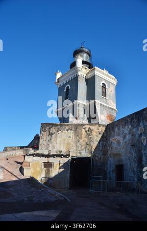 Ancient lighthouse stands tall against deep blue sky. Weathered stone walls show signs of time and wind. Open doorway invites exploration of historic Stock Photo