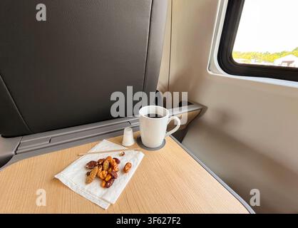 Coffee mug and pile of mixed nuts on napkin on train business class tray table Stock Photo