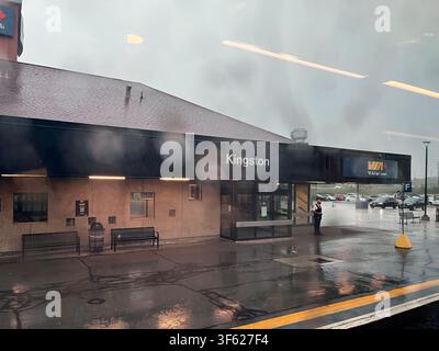 Ottawa, Ontario, Canada - June 30, 2026: View through rain-streaked window showing Kingston station building with wet platform, bench and VIA Rail sig Stock Photo
