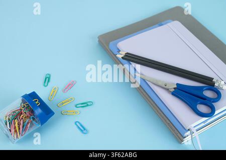 Two black pencils and blue scissors on a stack of notebooks with a small jar of colorful paper clips beside them Stock Photo