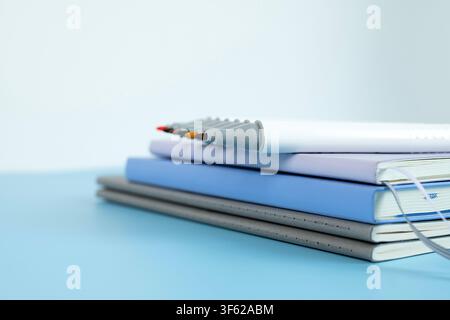 Stack of notebooks with colorful art markers arranged on top against a light blue background Stock Photo