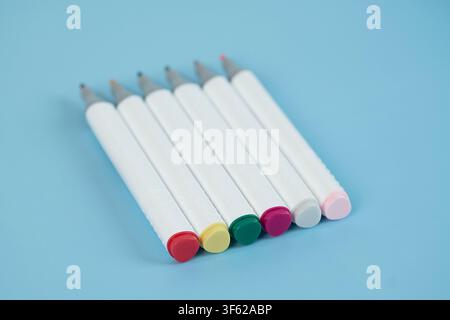 Stack of notebooks with colorful art markers arranged on top against a light blue background Stock Photo