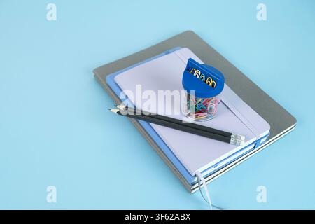 Two black pencils and a small transparent jar of colorful paper clips arranged on a stack of notebooks Stock Photo