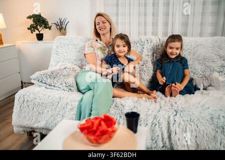 Mother and daughters relaxing on sofa watching TV at home Stock Photo