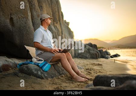 Man working on laptop at beach during sunset in Greece Stock Photo