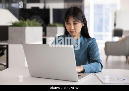 Serious Asian woman working on laptop in office Stock Photo