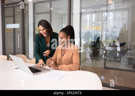 Smiling Hispanic woman explaining project details on laptop to colleague Stock Photo