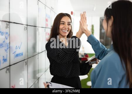 Two motivated professional women exchange high five at workplace Stock Photo