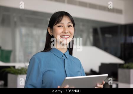 Portrait of smiling Asian business woman holding digital tablet Stock Photo