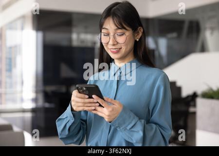 Smiling Asian businesswoman using smartphone in office Stock Photo