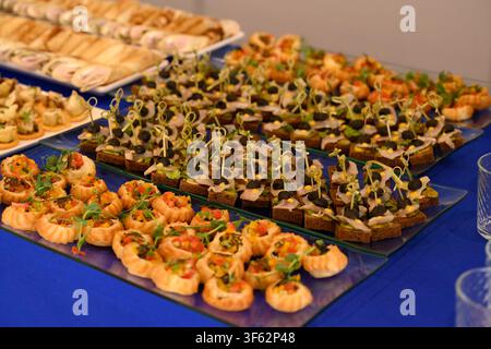 Assorted catering appetizer with herring fish canape on rye bread and vegetable puff pastry basket served on glass trays during a buffet banquet. Stock Photo