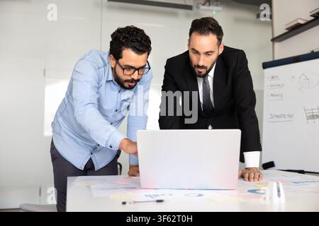 Multiethnic businessmen analyzing project data on laptop in corporate office Stock Photo