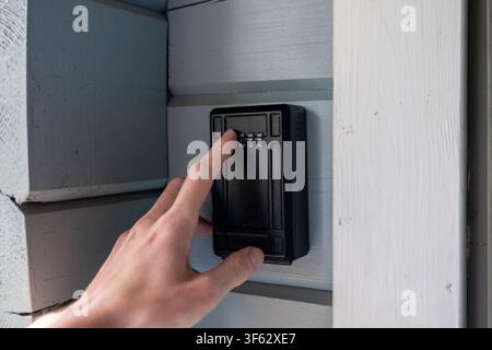 Person entering access code on secure outdoor key lock box mounted on wooden house wall for safe property access Stock Photo