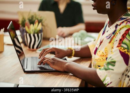 African American young woman typing on laptop keyboard in modern office. Image represents remote work and digital marketing, suitable for corporate communication, close up shot Stock Photo