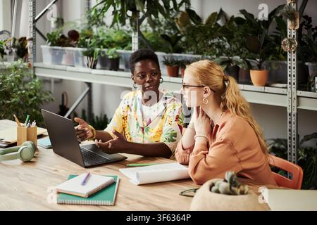 African American woman and Caucasian woman working together on laptop in green office. Diverse female colleagues collaborating on project, suitable for corporate diversity marketing Stock Photo