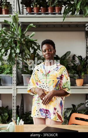 Portrait of young Black woman standing in plant nursery, smiling at camera. Image represents small business ownership and entrepreneurship, suitable for commercial marketing, vertical Stock Photo