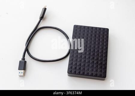 A black portable external hard drive and its connecting cable are placed on a white surface Stock Photo