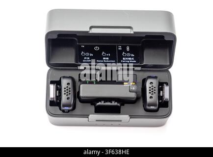 A wireless microphone set including transmitters and receiver sits neatly inside its open charging case against a plain white background Stock Photo