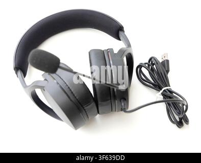 A pair of black wired headphones with an attached microphone and USB cable rests on a white background Stock Photo