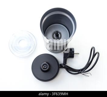 An electric milk frother is disassembled showing its main container with whisk, transparent lid, and powered base with cord on a white background Stock Photo
