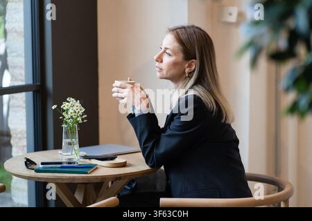Tired, thoughtful businesswoman on coffee break in cafe with laptop and smartphone, battling burnout Stock Photo