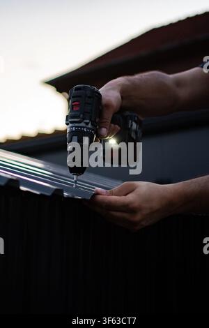 Worker using cordless drill on corrugated metal roof Stock Photo
