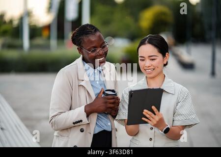 Diverse businesswomen checking tablet, discussing project outdoors Stock Photo