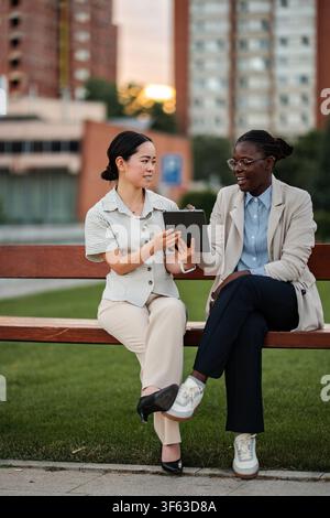 Diverse businesswomen collaborating with digital tablet on park bench Stock Photo