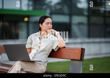 Asian businesswoman contemplating work project outdoors on bench Stock Photo