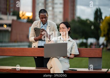 Two diverse businesswomen collaborating on a project using technology outdoors Stock Photo