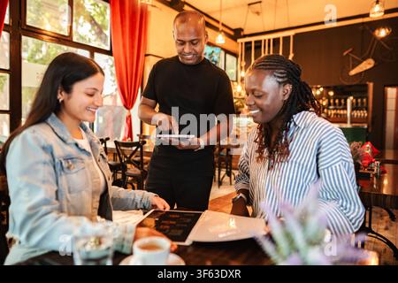 Waiter taking order from diverse women using a digital menu Stock Photo
