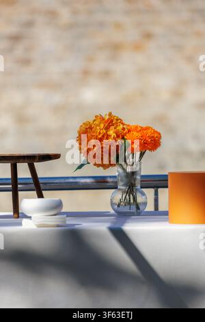 Orange Flowers in Glass Vase on Sunlit Outdoor Table with Copy Space Stock Photo