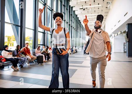 Excited couple pointing while walking through modern airport terminal Stock Photo