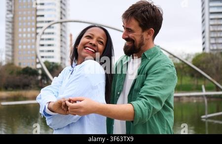 Happy multiracial couple dancing by lake in city park. Stock Photo