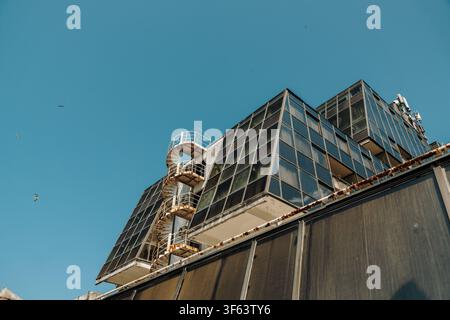 Contemporary glass facade featuring an exterior spiral staircase against a clear blue sky. Architectural detail with geometric lines and reflections. Stock Photo
