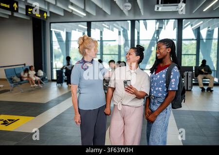 Diverse women friends talking in airport terminal while traveling Stock Photo